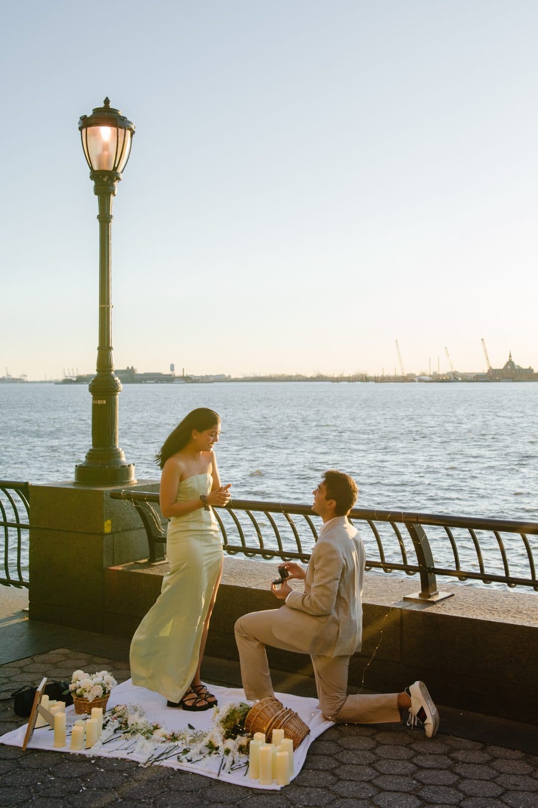 Shaan kneeling to propose to Krati beside the waterfront