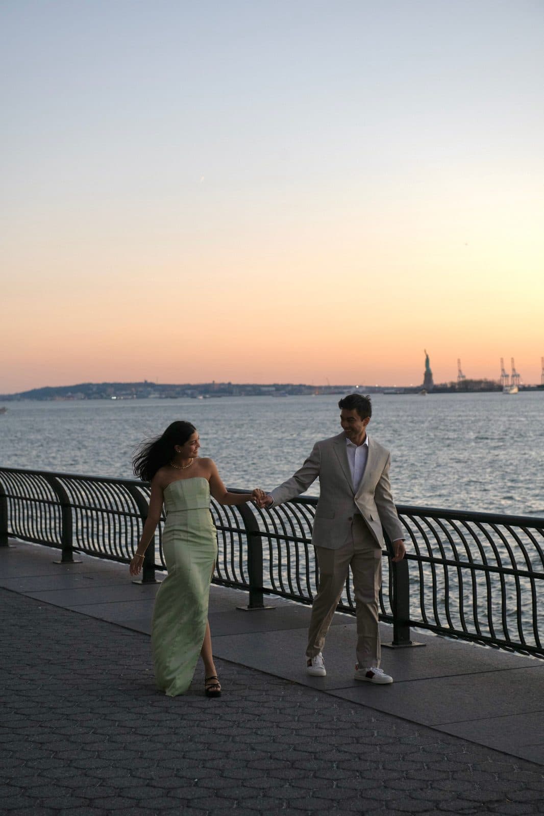 Krati and Shaan holding hands along the waterfront at dusk